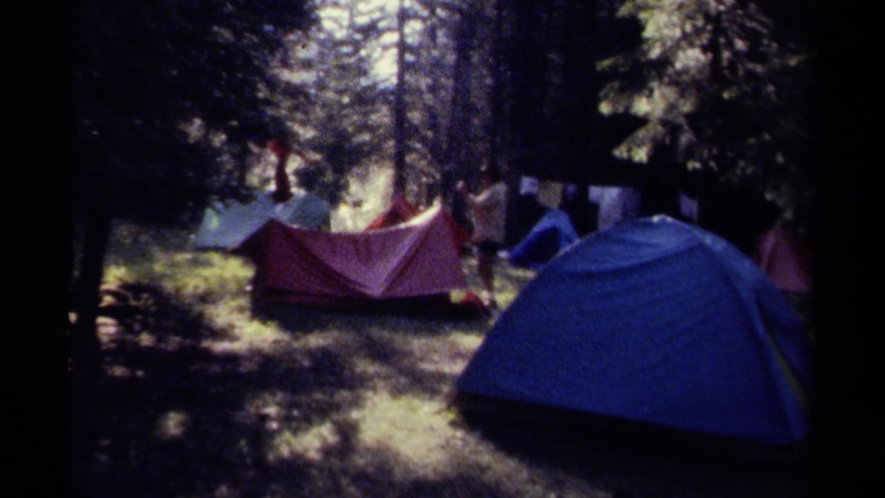 1979 British Columbia forest campsite with colorful tents and distant campers in an 8mm home-movie frame.