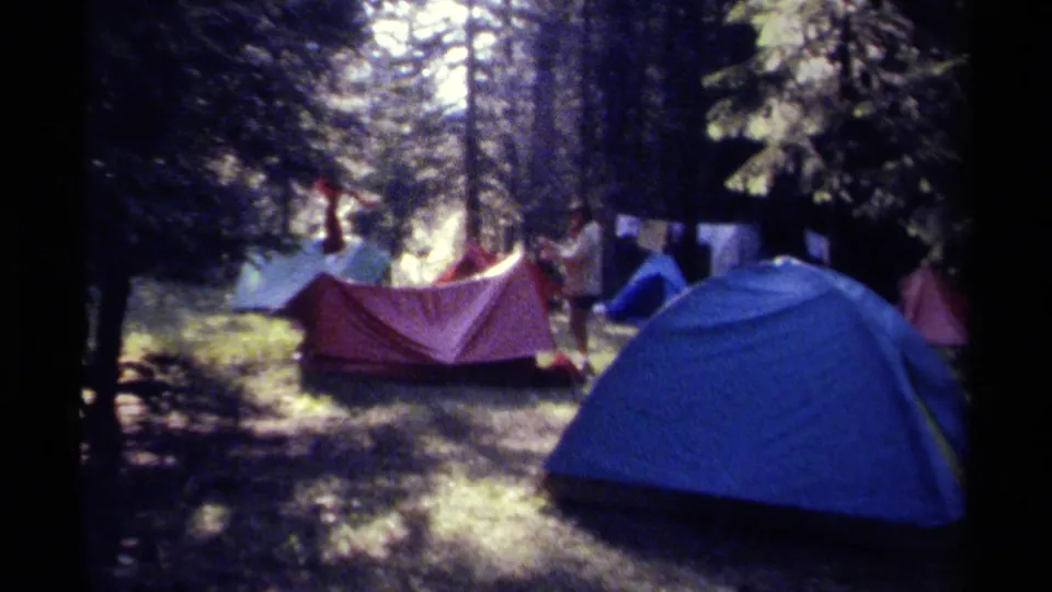 A blue foreground tent, red tent, and distant campers appear in a 1979 British Columbia forest campsite scene.