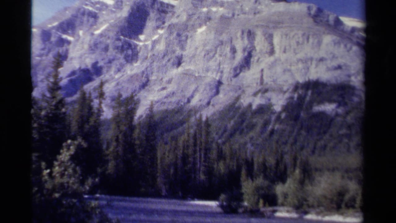 1979 British Columbia 8mm frame showing snow-dusted mountains, conifer forest, and a river valley from a handheld travel viewpoint.