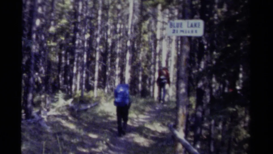 1979 British Columbia 8mm frame of hikers moving along a shaded forest trail near a sign reading Blue Lake 2 miles.