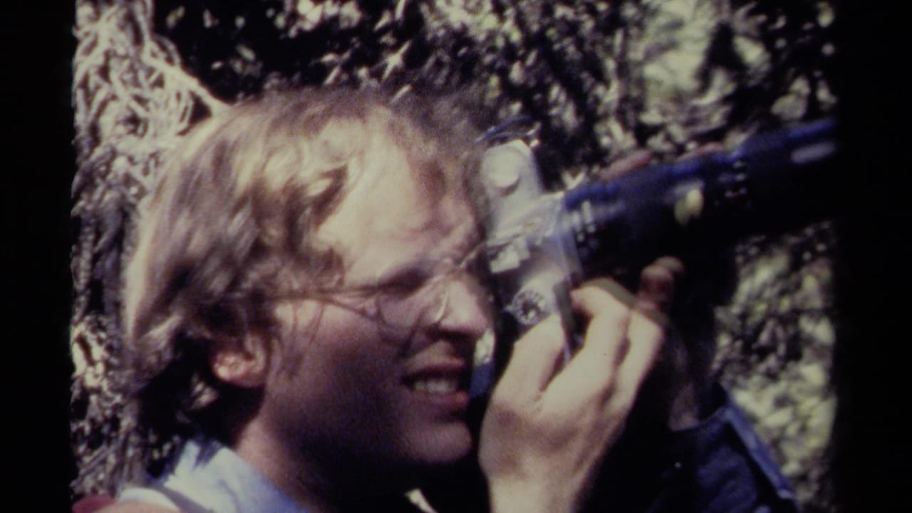 In 1979 British Columbia footage, a man with glasses operates a small movie camera beside textured tree branches.