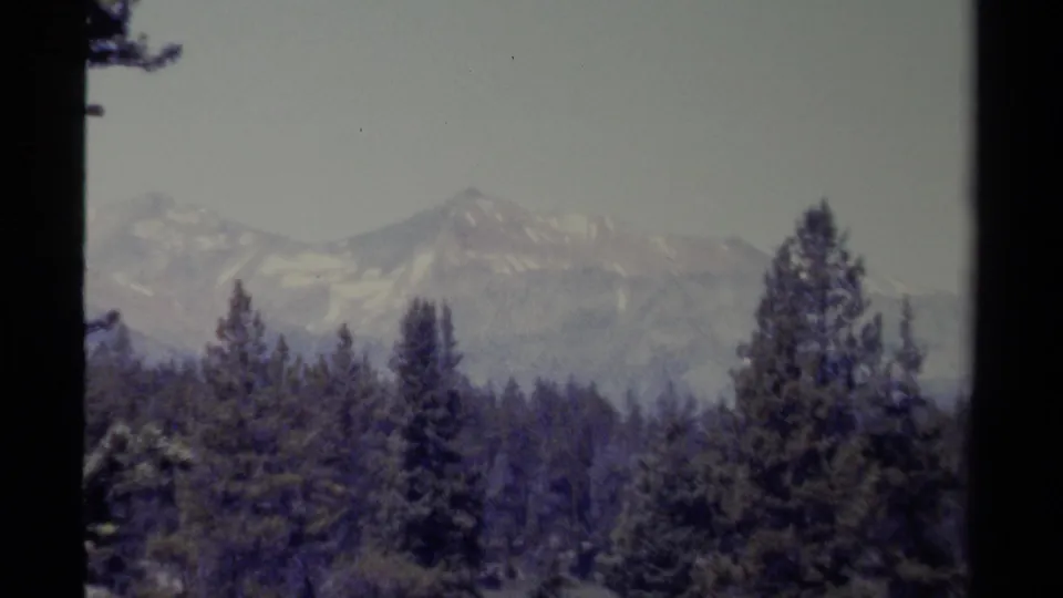 Snow-capped peaks and dark conifer trees fill a 1979 British Columbia home-movie landscape frame.