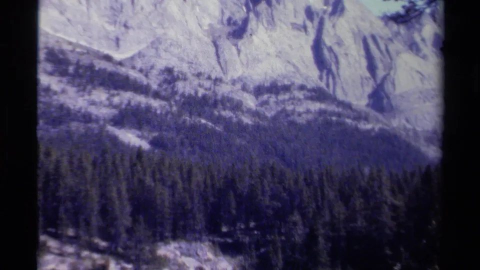 1979 8mm British Columbia mountain view with pale rocky ridges rising above a dense evergreen forest.