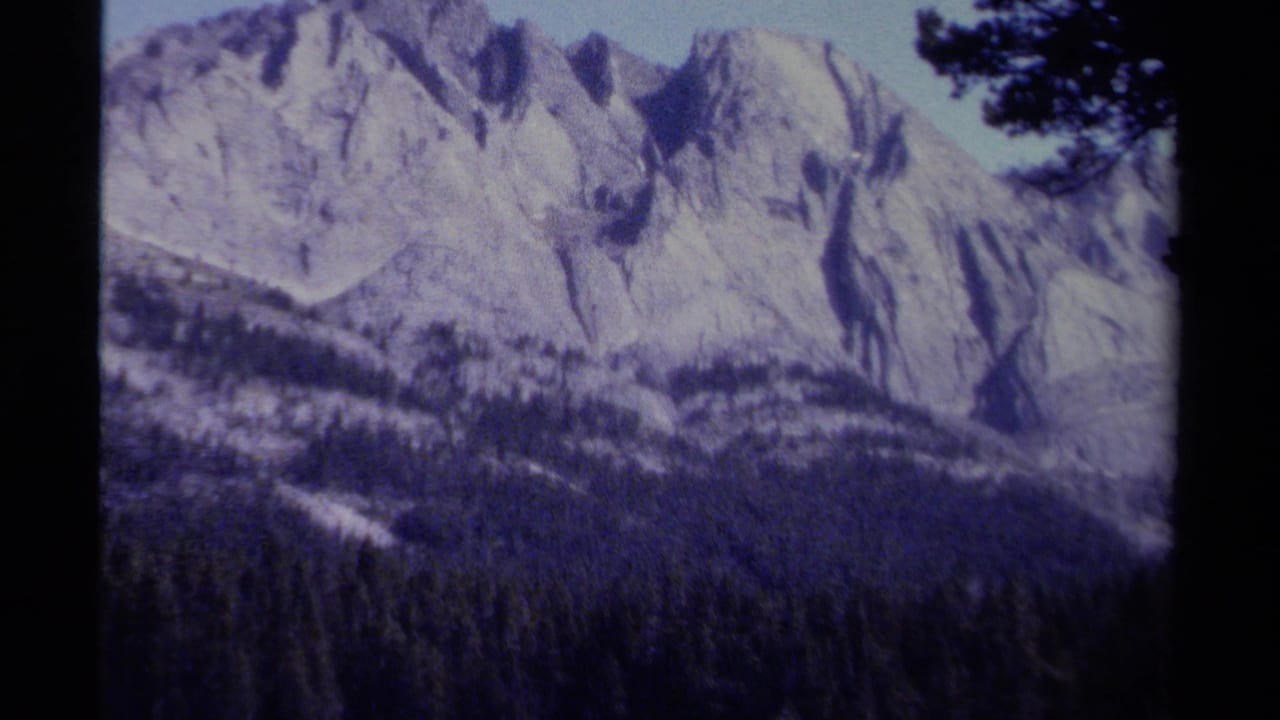 Aged 8mm view of British Columbia peaks with forested slopes and visible blue-purple color shift.