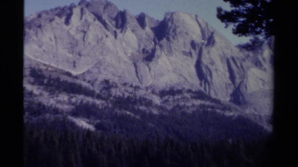 British Columbia mountain landscape on 8mm film, showing a broad rocky face behind dense evergreens.