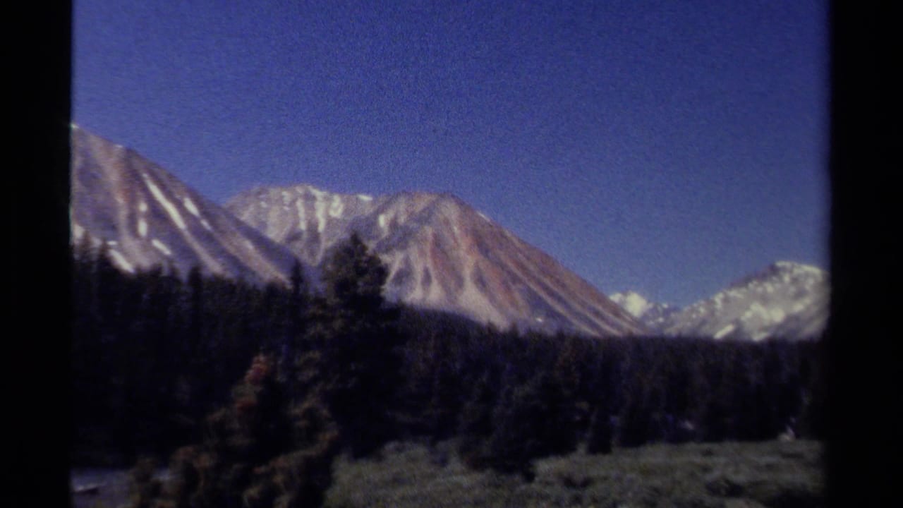 Mountain peaks and evergreen forest framed by dark vertical film edges.