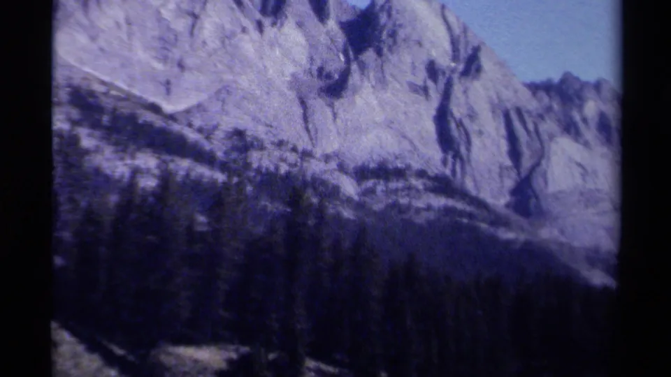 Archival 8mm view from British Columbia showing a rocky ridge, dark evergreen forest, and shadowed mountain slope.
