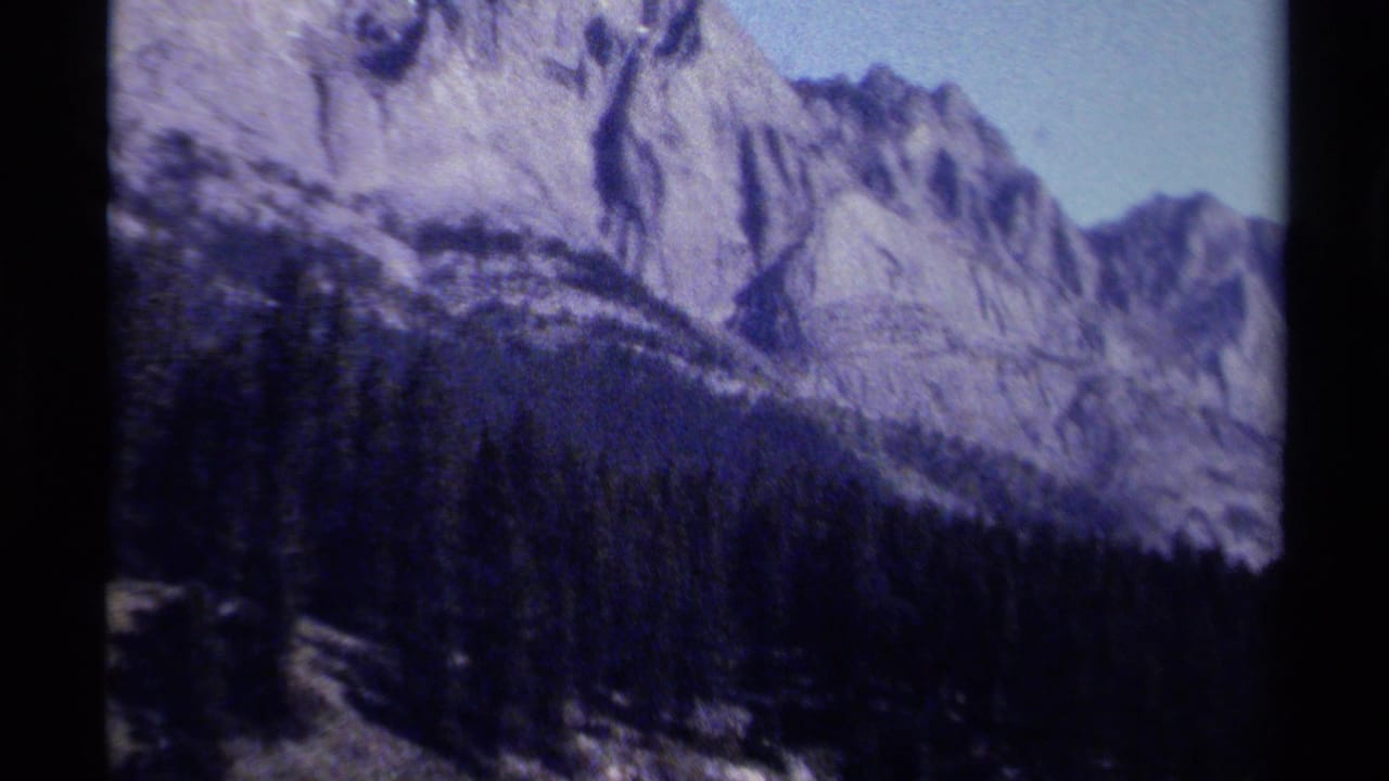 1979 8mm British Columbia mountain view with steep rock faces rising over a dense pine forest.