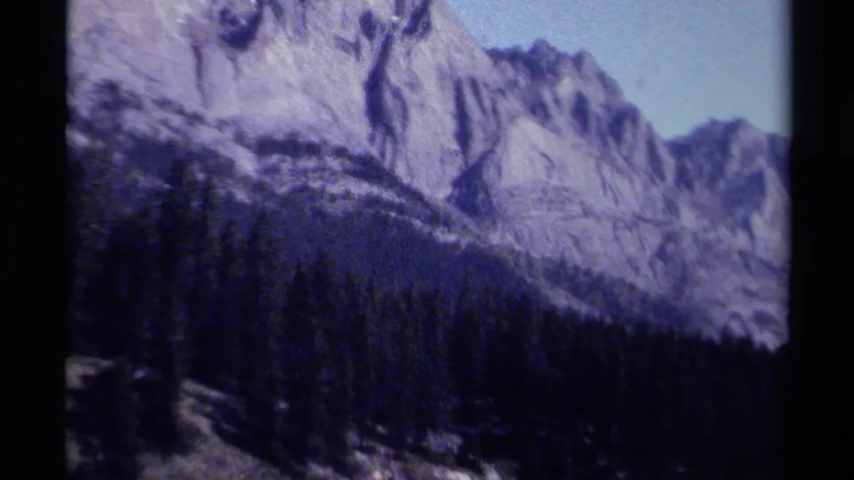 1979 8mm British Columbia mountain view with steep rock faces rising over a dense pine forest.