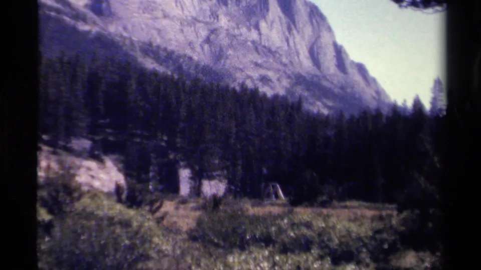 British Columbia 8mm frame showing a mountain forest backdrop with a grassy clearing and a small tent-like structure.