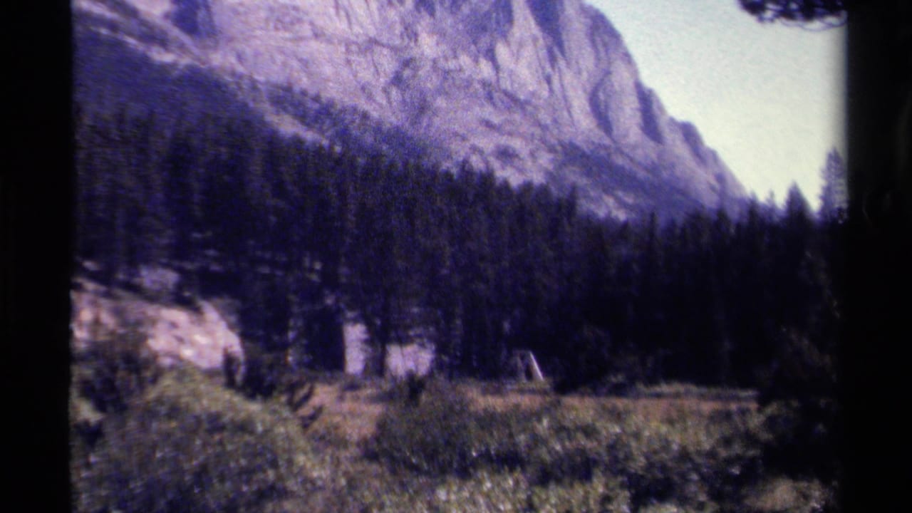 1979 British Columbia 8mm view of a forested mountain valley, with soft grain, dark frame edges, and a sunlit clearing below rocky slopes.