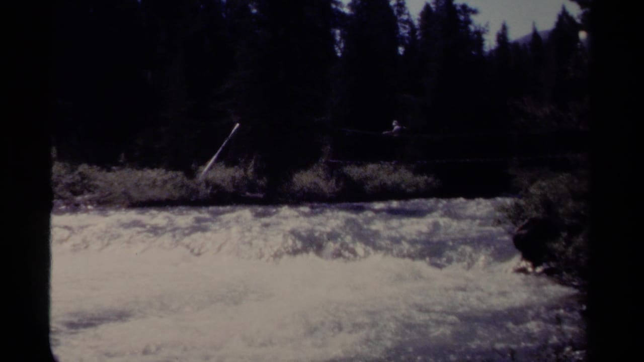 A distant person remains on the rope bridge above bright rushing water.