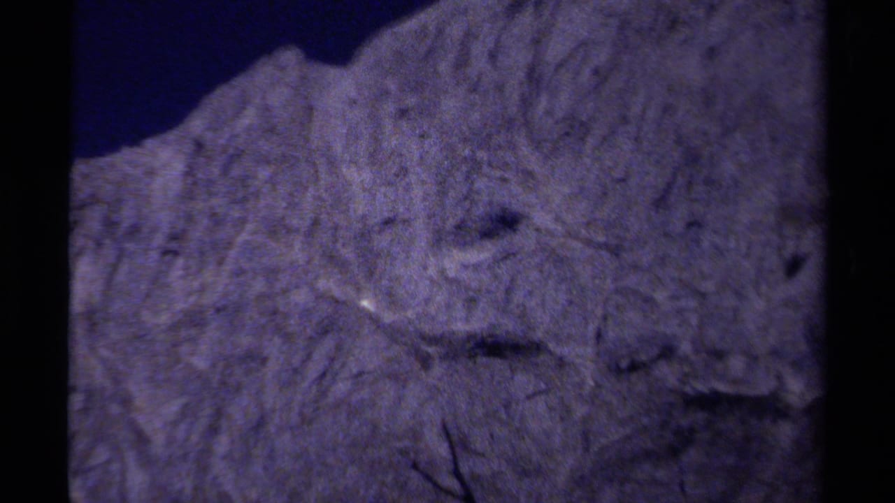1979 8mm British Columbia footage showing a soft, purple-shifted close view of rough mountain rock and shadowed crevices.