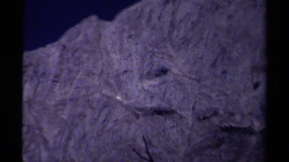 1979 8mm British Columbia footage showing a soft, purple-shifted close view of rough mountain rock and shadowed crevices.