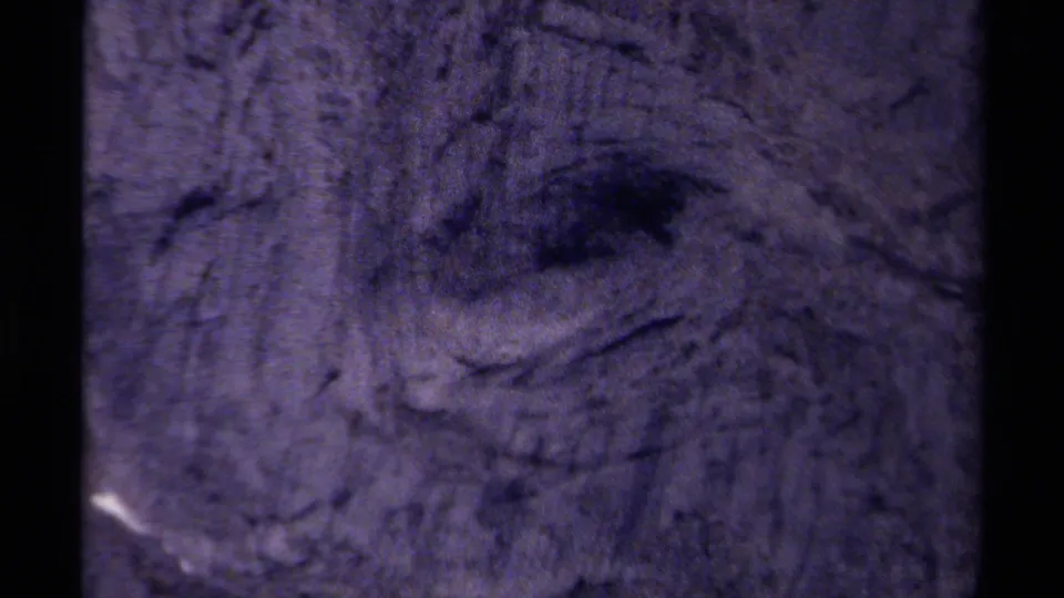 Grainy 1979 8mm frame of a shadowed rock hollow and rough stone surface in British Columbia mountain terrain.