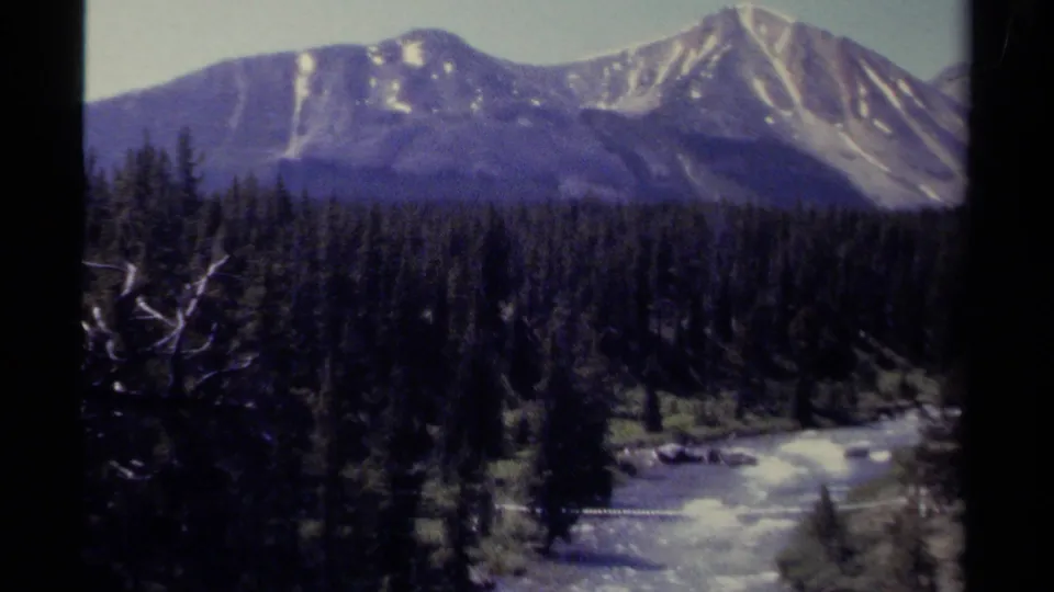 Wide 1979 British Columbia valley view with conifer forest, winding river, and snow-streaked mountain peaks.