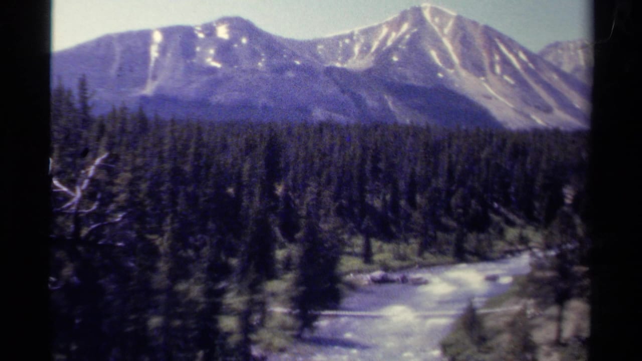 Snow-streaked mountains above evergreen forest and a winding river.