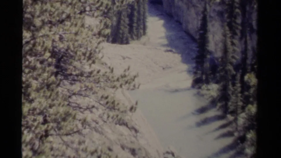 1979 8mm British Columbia view of a snowy river or creek corridor running through evergreen-lined canyon terrain.