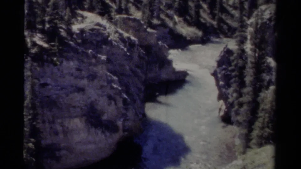 1979 British Columbia home-movie frame showing a narrow snowy river channel below rock walls and evergreen trees.