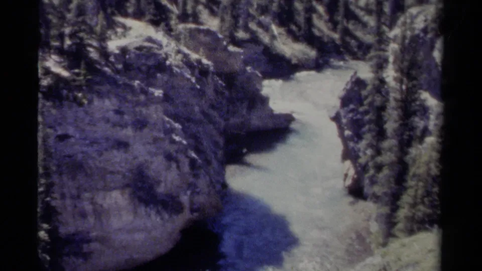 Vintage 8mm British Columbia frame of a snowy stream or river curving through a rocky evergreen canyon.