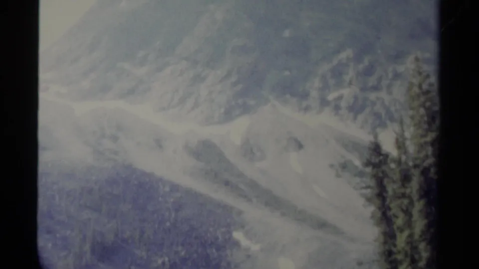 Distant British Columbia mountain scenery with snow patches and evergreens, captured in faded 1979 8mm color.