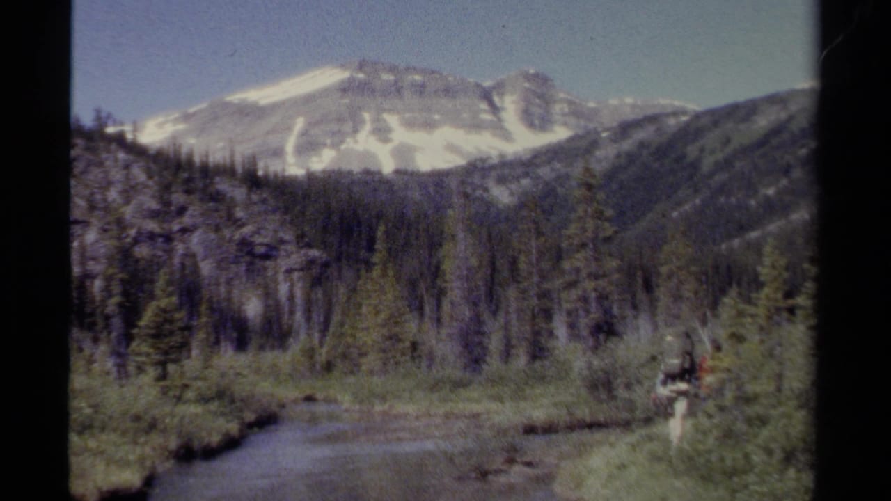1979 British Columbia 8mm frame showing a snow-capped mountain, forested valley, river bend, and a distant backpacked hiker.