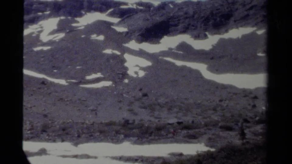 Vintage 8mm British Columbia mountain view showing rocky high terrain, bright snow patches, and faded blue-purple film color.