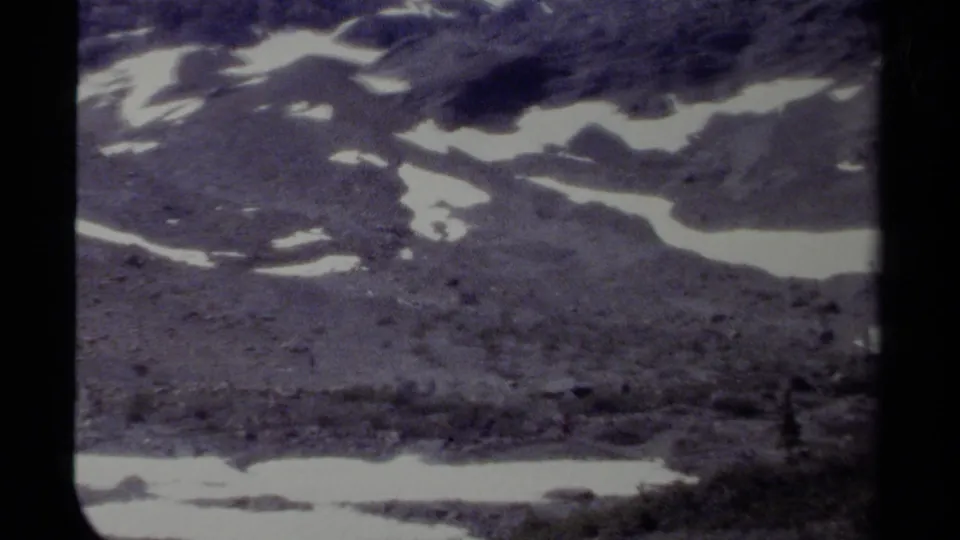 Closing 8mm view of British Columbia mountain snow patches across dark rock, framed by heavy gate borders and soft archival grain.