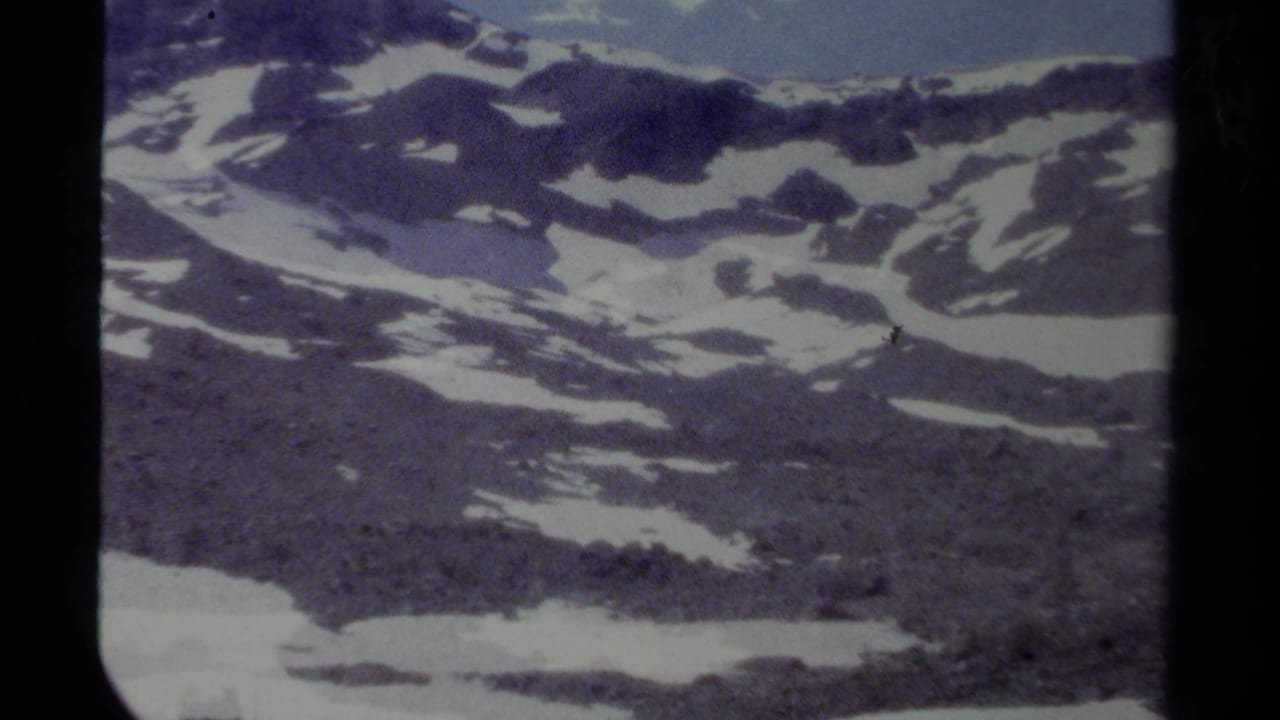 Snow-patched rocky mountain slopes beneath a pale blue sky.