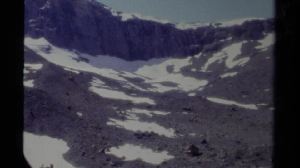 1979 British Columbia mountain view with a jagged dark ridge, scattered snowfields, and visible 8mm scan texture.