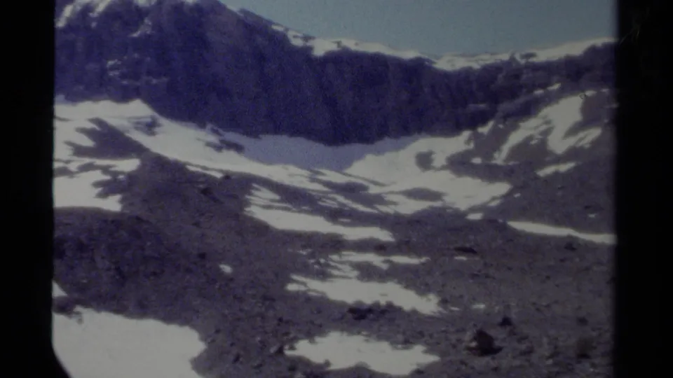 1979 British Columbia 8mm view across a rocky mountain basin with lingering snow and a dark ridge in the distance.