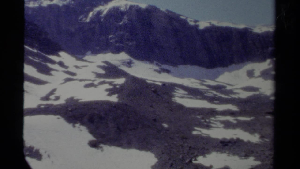 1979 British Columbia 8mm frame showing a distant rocky mountain ridge with snow patches and a pale blue sky.