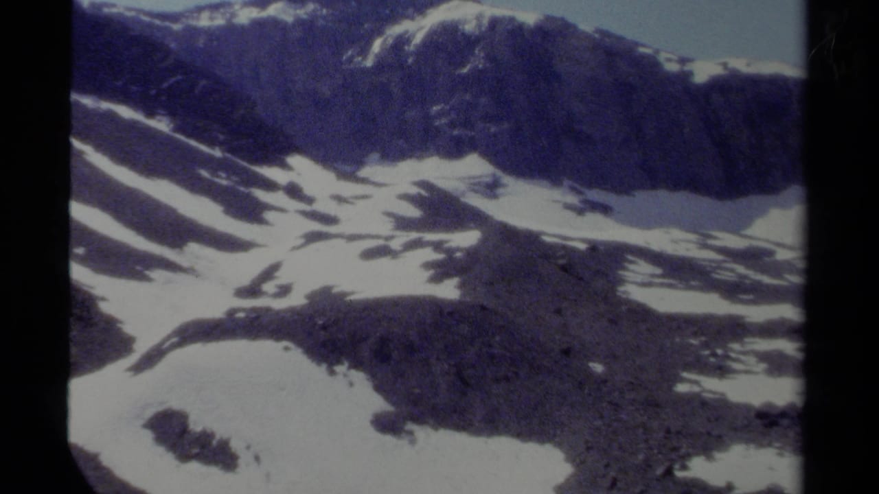 1979 British Columbia 8mm frame of a rugged mountain slope with scattered snowfields and soft analog color.