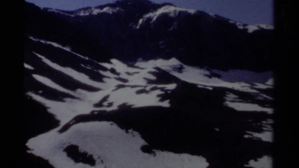 1979 British Columbia 8mm frame showing shadowed alpine terrain, white snow bands, and pronounced film grain.