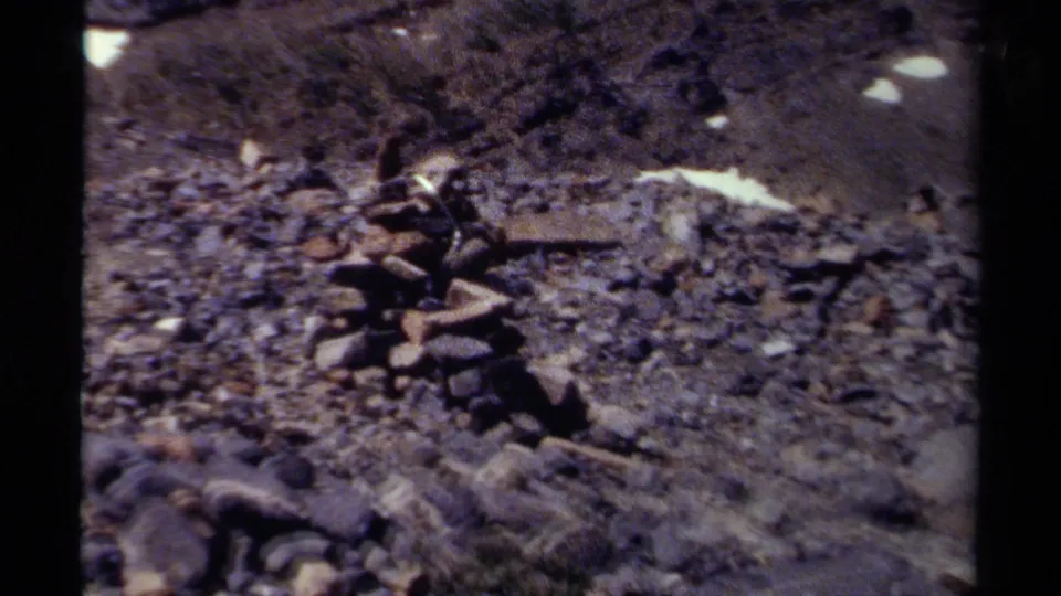 1979 British Columbia 8mm frame moving closer to a stone cairn on rough gravel with snow visible higher on the slope.