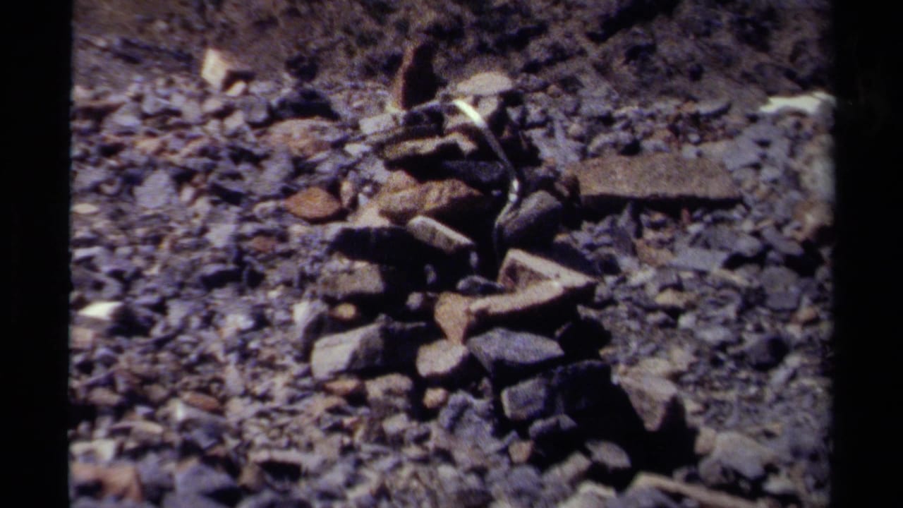 1979 British Columbia 8mm frame showing a small stone cairn on rough rocky terrain.