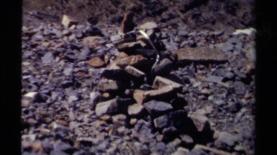 1979 British Columbia 8mm frame showing a small stone cairn on rough rocky terrain.