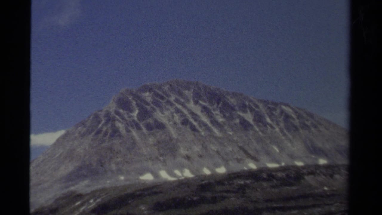 Rounded mountain peak beneath a deep blue sky with snow patches below.