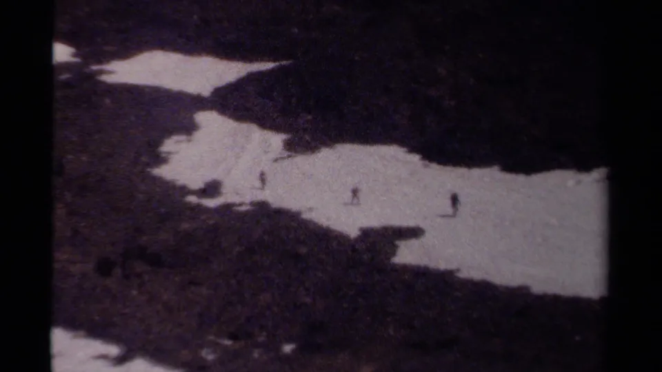1979 British Columbia home-movie frame showing small hikers moving across snow and exposed alpine ground.