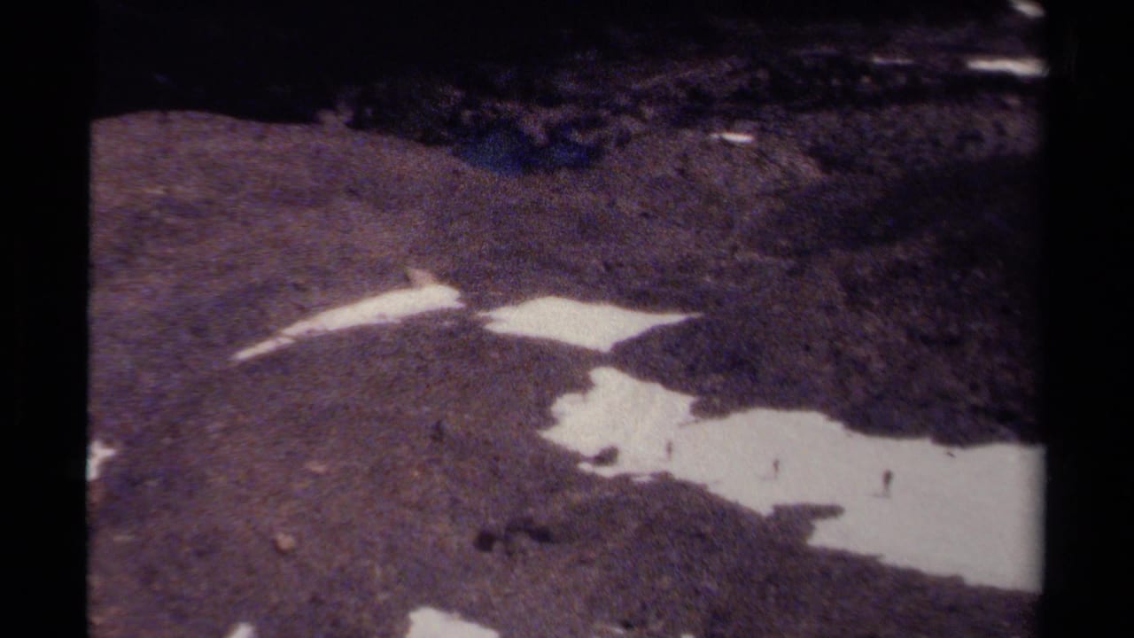 Small hikers are visible near irregular snow patches on rugged British Columbia mountain terrain.