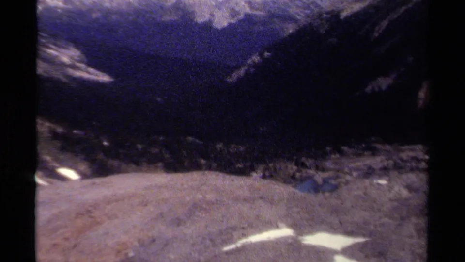 Handheld 1979 British Columbia footage looks from snowy alpine ground toward a shadowed mountain valley.