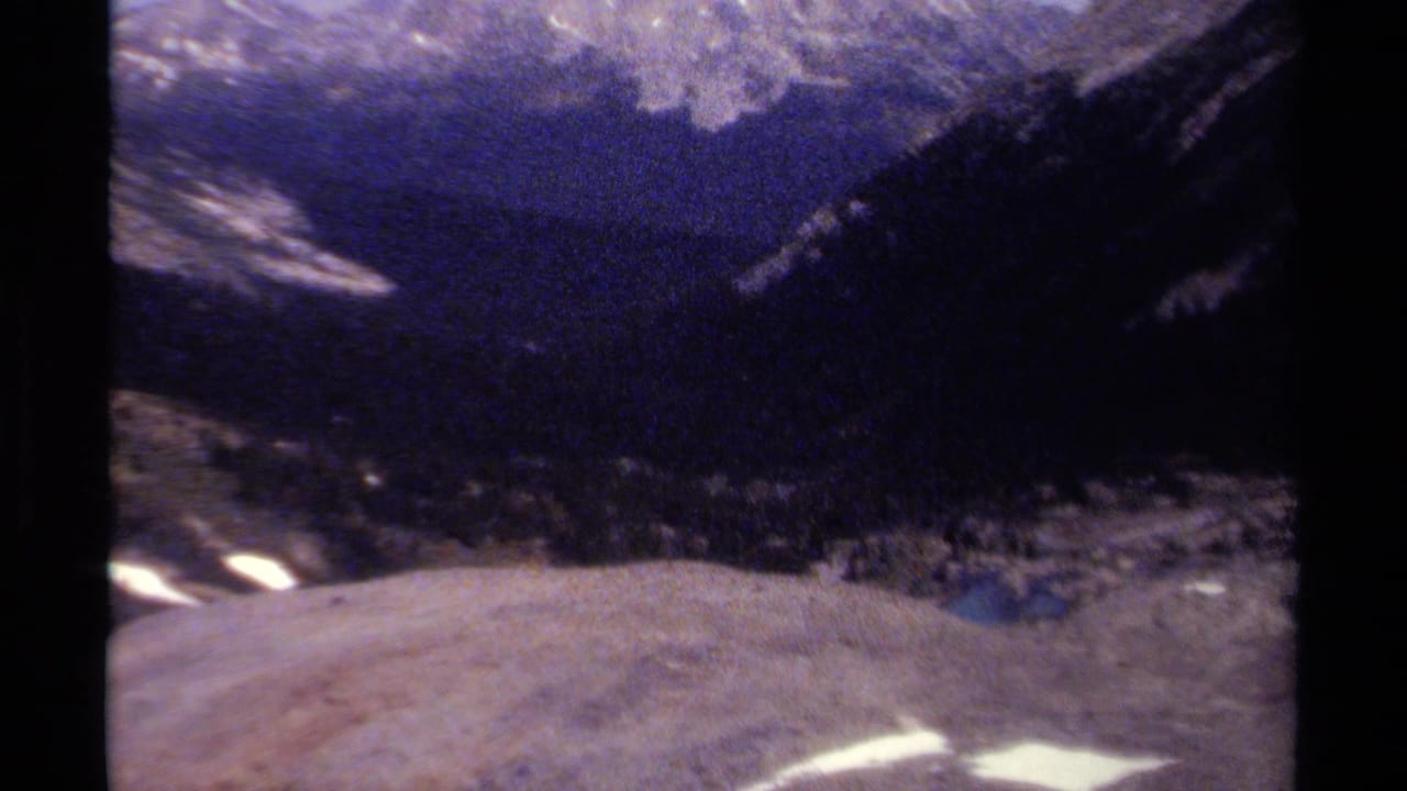 Dark, grainy mountain valley view with snow patches and black film borders.