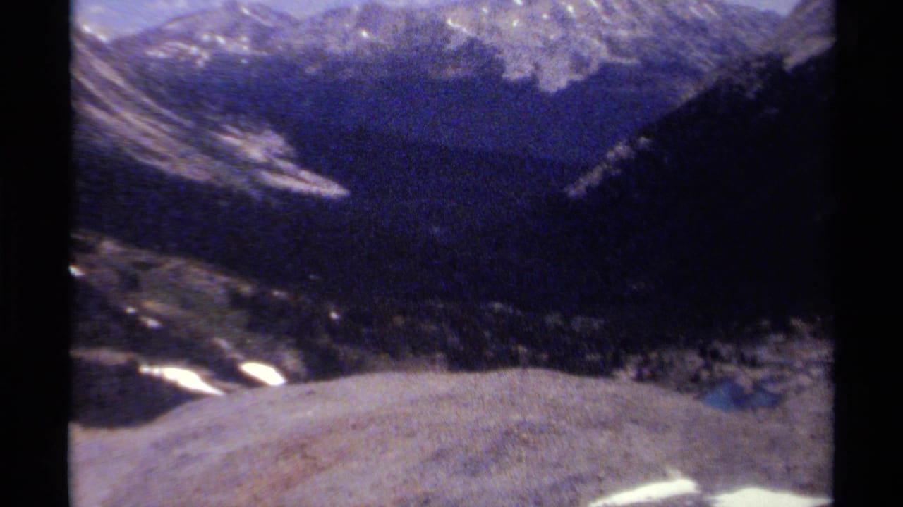 Soft 1979 8mm view of a British Columbia mountain range, with dark ridges, snow patches, and visible frame edges.