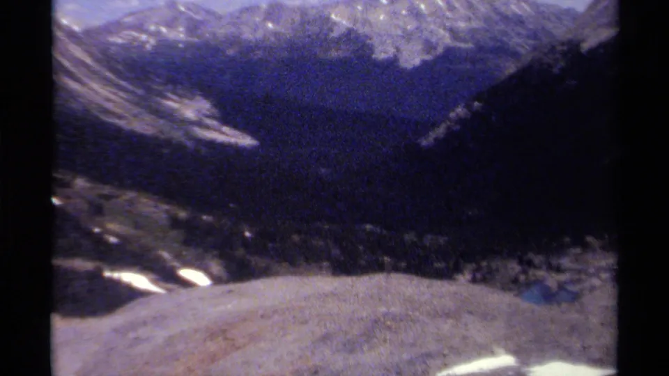 Soft 1979 8mm view of a British Columbia mountain range, with dark ridges, snow patches, and visible frame edges.