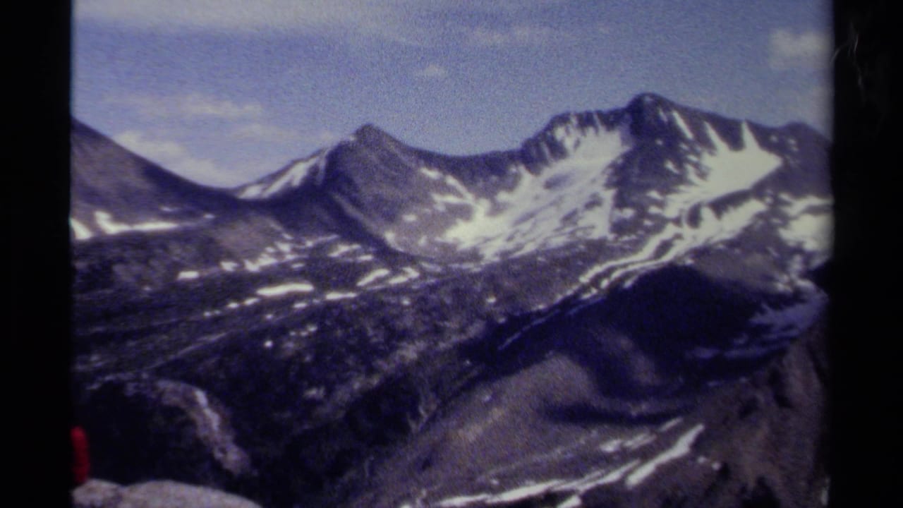 1979 8mm home-movie view of British Columbia alpine peaks with snow patches, rocky slopes, blue sky, and visible film gate edges.