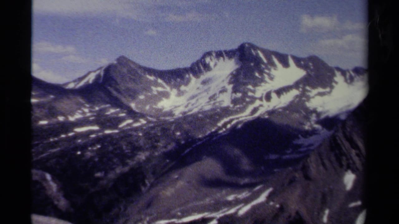 Broad alpine mountain view with snowfields, rocky ridges, and blue sky.