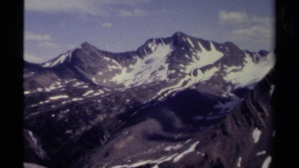 1979 British Columbia home-movie frame of a rugged mountain ridge with snow patches, muted clouds, and small-gauge film texture.