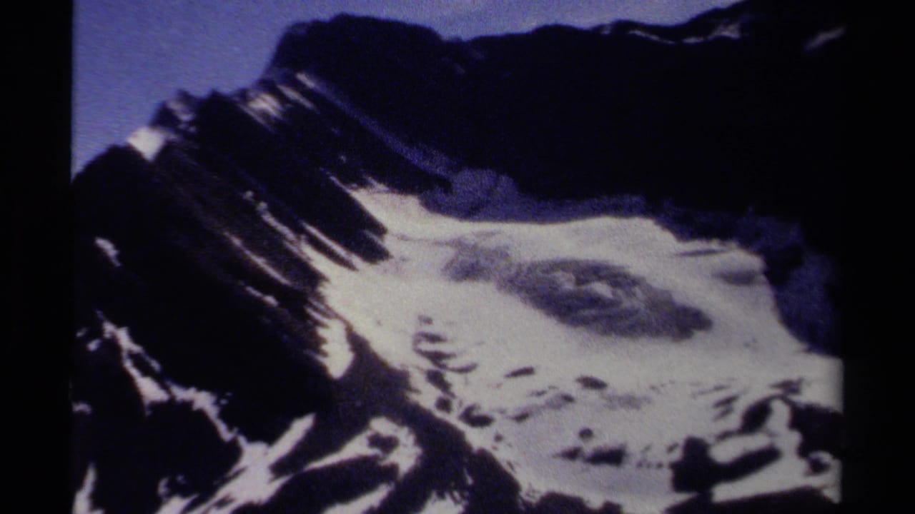 The frame shows a rugged snow-dusted mountain face in British Columbia, with deep shadows and saturated blue 8mm color.