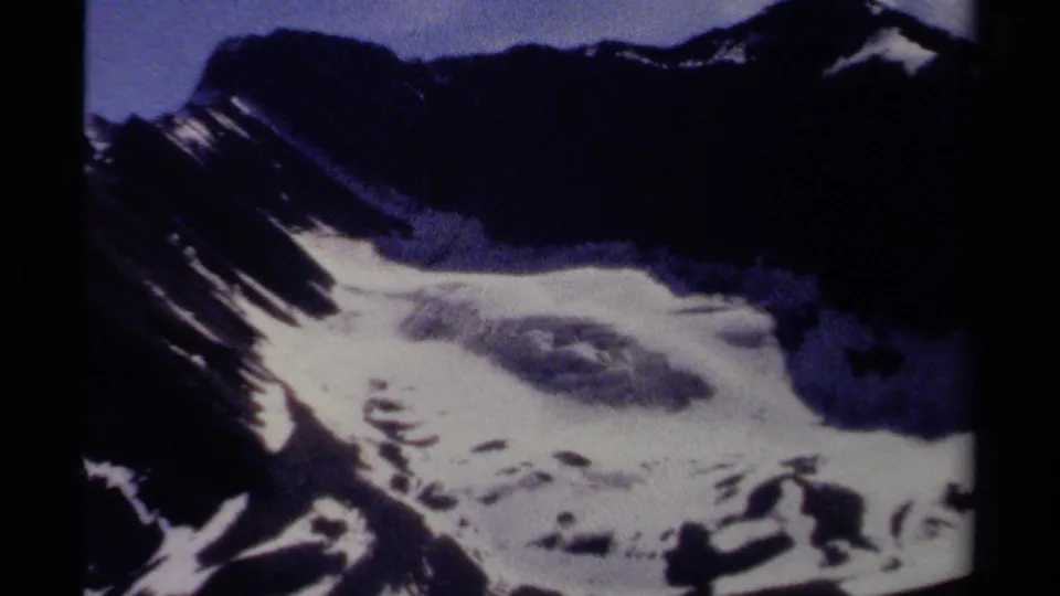 A slightly reframed 1979 8mm view of a British Columbia alpine slope, showing snow against dark rock and a small area of sky.