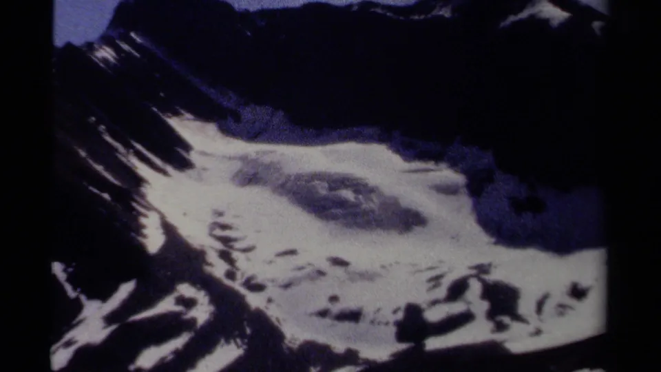 The final frame keeps the British Columbia mountain face in view, with bright snow, dark cliff areas, and cool-toned 8mm grain.